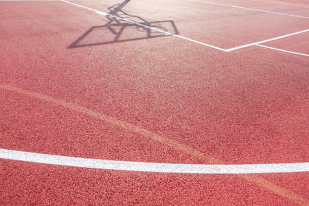 White lines on outdoor basketball field and shadow of the rack with a shield and basketball ring...