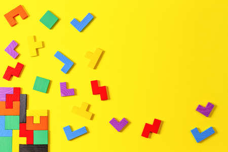 Different colorful shapes wooden puzzle blocks on yellow background. Geometric shapes in different...