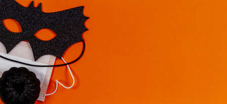 Black halloween eye mask, little black pumpkin and medical protective face mask on orange backgroundの写真素材