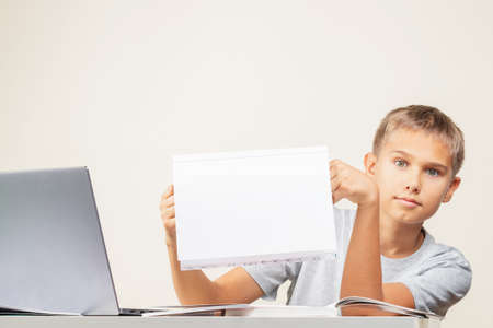 Kid hands holding open notebook with blank white pages Boy sitting at table with books and laptop...