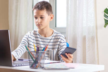 Kid sitting with laptop computer and scrolling phone instead of doing homework. Technology, online...