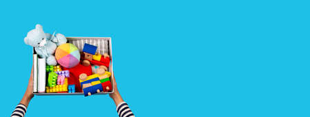 Donation concept. Kid hands with donate box with clothes, books and toys on light blue background. Top viewの写真素材