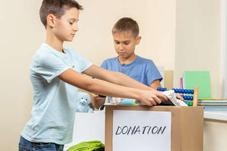 Kids volunteers sorting toys, clothes, books, donation goods in donate charity boxes
