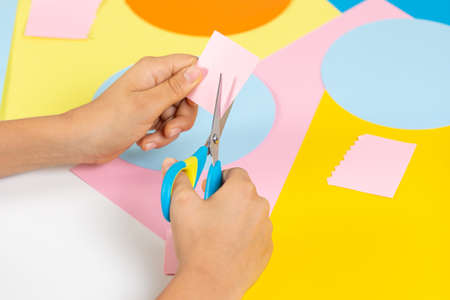 Kid hands cutting colored paper with scissors. Education, learning, paper craft, entertainment at homeの写真素材
