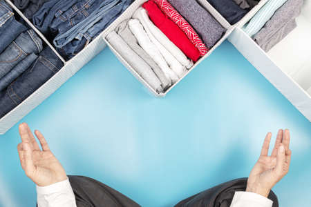 Woman hands sitting in lotus pose, meditating, while cleaning home, sorting and tidying up clothes....