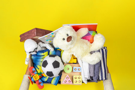 Donation box with baby kid toys, books, school supplies, clothing for charity on yellow background. Top viewの写真素材