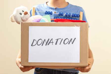 Donation concept. Volunteer hands holding donate box with clothes, books and toys for charityの写真素材