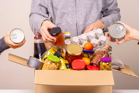 Volunteers hands collecting grocery products, foodstuff to food donations boxの写真素材