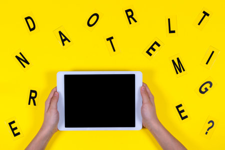Top view to kid hand holding digital tablet and letters on yellow background. Online learning, home...
