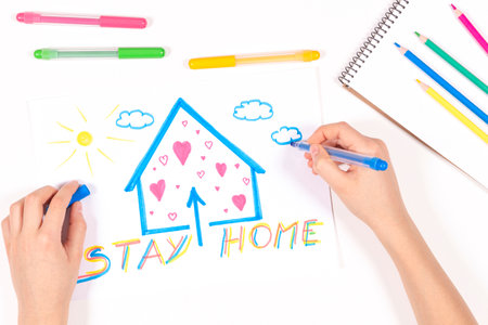 Stay at home. Kid hands drawing picture with house and message Stay home. Top view. Quarantine during coronavirus pandemicの写真素材