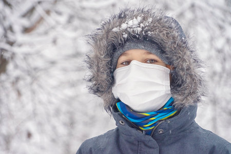 Kid boy wearing medical protective mask having fun outdoors. Active winter leisure, entertainment during corona virus pandemic lockdownの写真素材