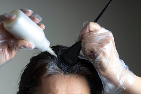 Closeup woman hands dyeing hair using black brush. Middle age woman colouring dark hair with gray roots at homeの写真素材