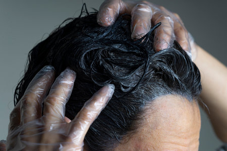 Closeup woman hands dyeing hair. Middle age woman colouring dark hair with gray roots at homeの写真素材