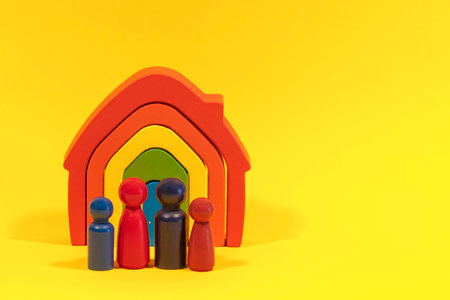 Wooden figures, miniature people standing in front of rainbow color house on yellow background. Family with children, stay home, real estate conceptの写真素材