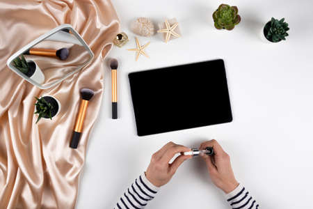 Make up, beauty blogger, online learning composition background. Female hands, cosmetics, make up brushes, digital tablet on white desk. Top viewの写真素材