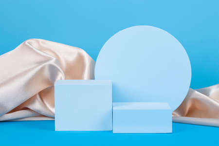 Geometric podium on light blue background with draped champagne color silk cloth. Empty showcase for cosmetic product presentation, promotion saleの写真素材