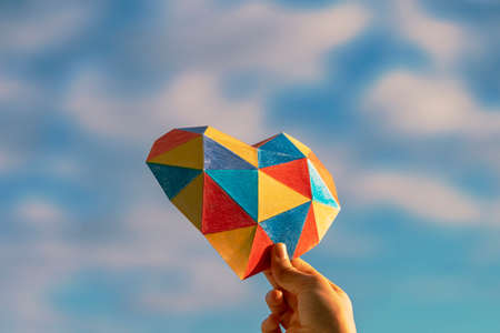 Child hands holding colorful heart over blue sky background. World autism awareness day conceptの写真素材