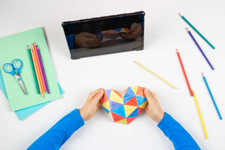 Top view to child hands holding colorful heart. Digital tablet, colored pencils on white desk. World autism awareness day conceptの写真素材