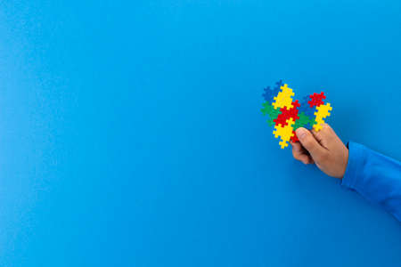 World autism awareness day concept. Child hand holding colorful puzzle heart on light blue backgroundの写真素材