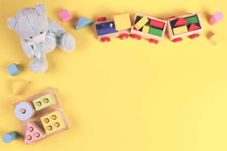 Baby kids toys background. Teddy bear, wooden educational toys and bricks on yellow background. Top view, flat layの写真素材