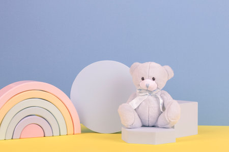 Baby kid toy background. Blue teddy bear, colorful wooden rainbow and geometric shapes podium platform on light blue and yellow backgroundの写真素材