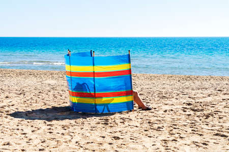 Two people relaxing behind colorful striped windscreen on the beach near the seaの写真素材