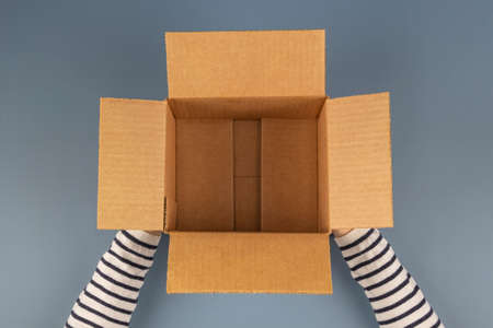Female hands with empty open cardboard box on gray background. Top view