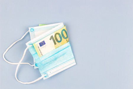 Disposable protective medical face masks folded with one hundred euro banknote on gray background. Top viewの写真素材