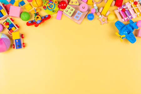 Baby kids toys frame. Colorful educational wooden plastic and fluffy toys for children on pastel yellow background. Top view, flat layの写真素材