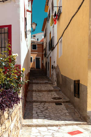 Finestrat, Alicante province, Spain. Beautiful quiet narrow street of small Finestrat village old town with old buildings, stone pavement at sunny dayの写真素材