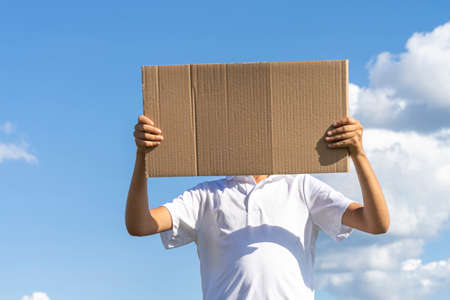 Boy holding with two hands brown paper cardboard outdoors with blue sky backgroundの写真素材