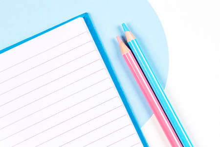 Light blue and pink colored pencils with open notebook on geometric blue and white background. Top view.の写真素材