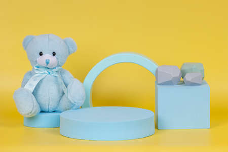 Creative baby kid toy background. Blue teddy bear and geometric shapes podium platform on yellow backgroundの写真素材