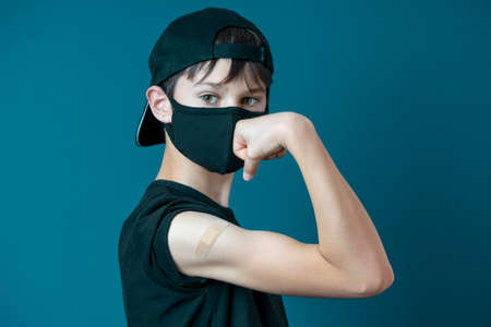 Teenage boy with bandage plaster on his arm makes fist and flexes her bicep after vaccination.