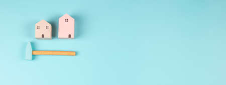 Small wooden houses and hummer on light blue background. New house construction, repair maintenance,...