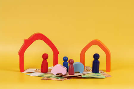 Divorce, conflict between parents, children custody, property division. Wooden houses, miniature figures of parents and children, cash money on yellow backgroundの写真素材