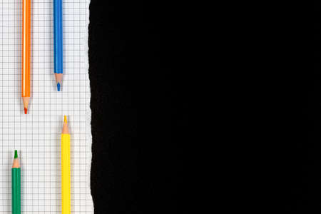 Colored pencils on white squared torn sheet of paper over black school chalkboard blackboard. Back to school, learning concept. Top view, copy spaceの写真素材