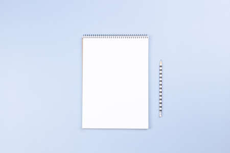 Open spiral notebook with blank white page and pencil on light gray desk background. Top view, copy...