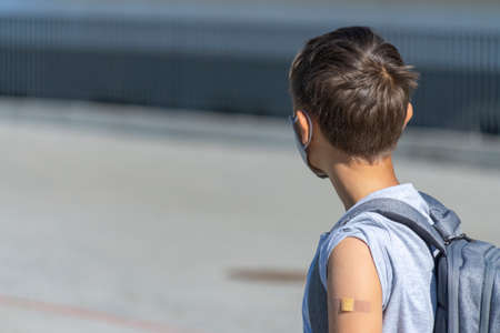 Teenage boy in protective mask with adhesive bandage plaster on his arm walk to school. Back to school, vaccination, travel conceptの写真素材