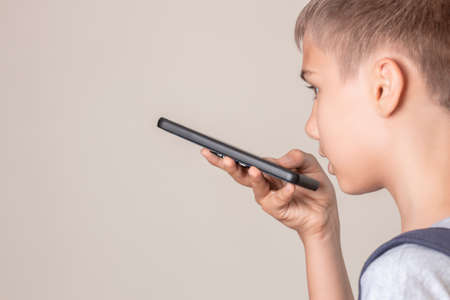 Teenage boy hold smart phone talking through microphone, using cell phone voice recognition function online, sending record voice messageの写真素材