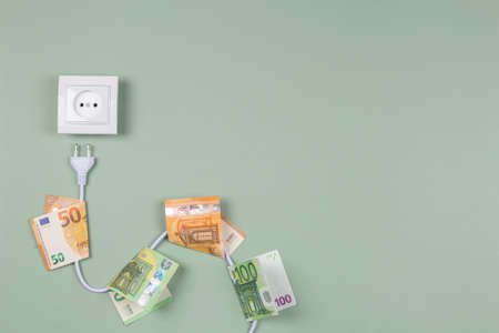 Electric power plug with euro banknotes on it and electric socket on light green background. Electricity cost and expensive energy conceptの写真素材