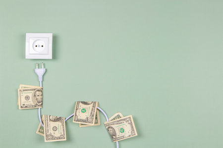 Electric power plug with US dollars banknotes on it and electric socket on light green background. Electricity cost and expensive energy conceptの写真素材