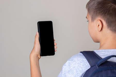Teenage boy holding cell phone, looking at screen, reading, watching video, listening voice message. Rear viewの写真素材