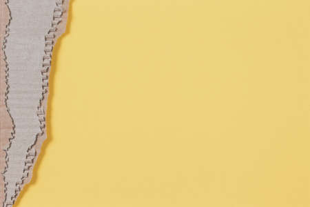 Old brown corrugated cardboard piece with ragged edge on pastel yellow backgroundの写真素材