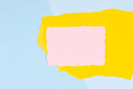 Torn paper textured collage background. Grunge ripped pastel paper piece with ragged edge on light blue and yellow paper backgroundの写真素材