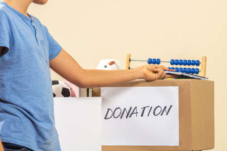 Kid collecting and putting toys, clothes, books, donation goods in donate charity boxes