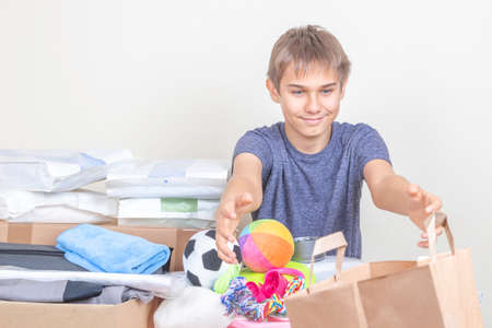 Teenage boy extending hands, stretching out arms to take bag with donation. Volunteer collecting pet...