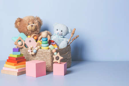 Toy box full of baby kid toys. Container with teddy bear, wooden rattles, stacking pyramid and wood blocks on light blue background. Cute toys collection for small children. Donatation. Front viewの写真素材
