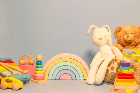 Toys background. Toy box with teddy bear, bunny and wood rattle. Educational wooden Montessori toys on pastel blue background. Cute toys collection for small children. Front viewの写真素材