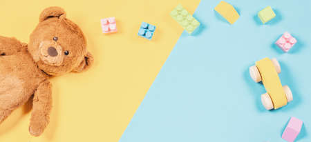 Baby kids toys banner background. Cute teddy bear, wooden toy car, colorful bricks on blue and yellow background. Top viewの写真素材